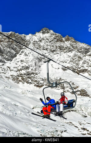 Skiers on a chairlift against the Fee Glacier and the peak Lenzspitze, Mischabel massif, skiing area Saas-Fee, Valais, Switzerland Stock Photo