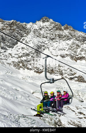 Skiers on a chairlift against the Fee Glacier and the peak Lenzspitze, Mischabel massif, skiing area Saas-Fee, Valais, Switzerland Stock Photo