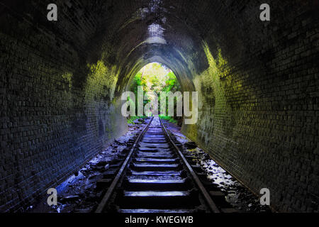 Old abandoned railway tunnel facing towards lush evergreen jungle in Helensburgh regional town of NSW, Australia. Exit portal letting sun light in ref Stock Photo