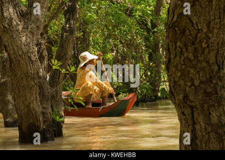 Asian Cambodian woman wearing yellow and a hat paddling a canoe, exploring floating forest flooded forest in Kampong Phluk, Tonle Sap Lake Cambodia Stock Photo