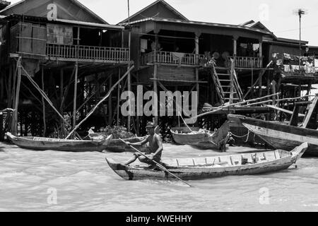 A Cambodian Asian brown skinned man rowing a wooden boat in Kampong Phluk Tone Sap Great Lake floodplain village on stilts, near Siem Reap, Cambodia Stock Photo