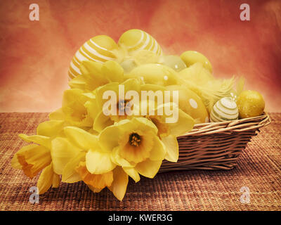 Still life of easter basket decorated with flowers and eggs on wicker table mat against pink textured wallpaper Stock Photo