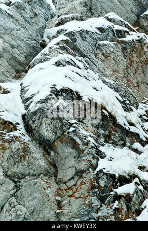 vertical background: a fragment of the wall of a natural cliff with snow-covered ledges Stock Photo