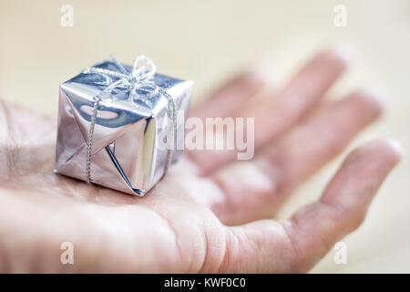 A small gift packed on male hands. Decoration for a Christmas tree on the palm of your hand. Black background. Stock Photo