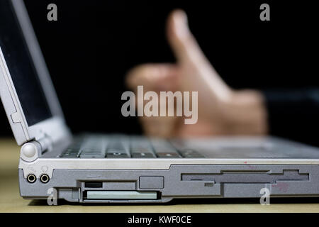 A laptop on a wooden table as seen from a profile with a hand. Computer keyboard with a hand raised above the keyboard. Black background. Stock Photo