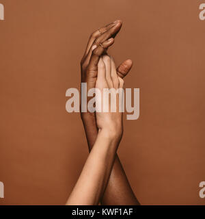 Close up of two female hands together on brown background. Hands of african and caucasian female. Stock Photo