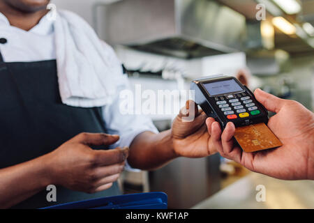 Hands of customer paying restaurant bill using credit card. Customer making payment through credit card at counter in a restaurant. Stock Photo