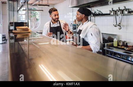 Two male cooks wearing uniform working in commercial kitchen. Professional chefs discussing the taste of new dish they cooked together in restaurant k Stock Photo