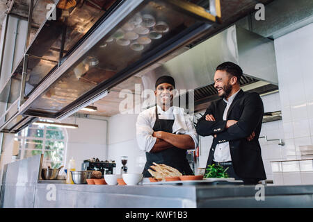 Smiling restaurant owner and chef standing in kitchen. businessman with professional cook standing together and laughing. Stock Photo