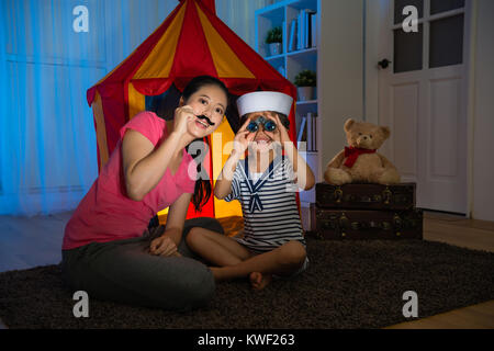 happy beauty girl children as sailor using telescope looking for treasure when she playing game with mother in bedroom at evening. Stock Photo