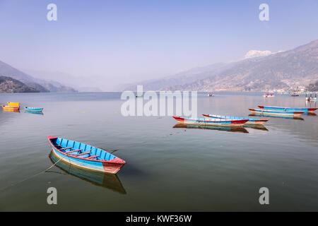 Traditional wooden rowbaots in Phewa lake in Pokhara, at the feet of the Annapurna mountain range in Nepal in South Asia. Stock Photo