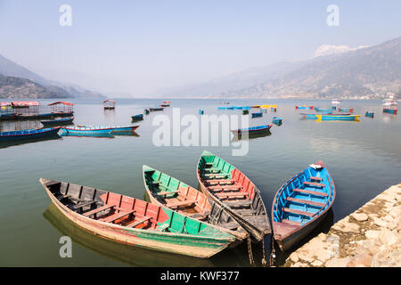 Traditional wooden rowbaots in Phewa lake in Pokhara, at the feet of the Annapurna mountain range in Nepal in South Asia. Stock Photo