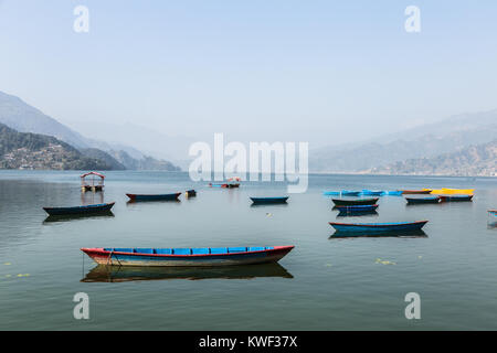 Traditional wooden rowbaots in Phewa lake in Pokhara, at the feet of the Annapurna mountain range in Nepal in South Asia. Stock Photo