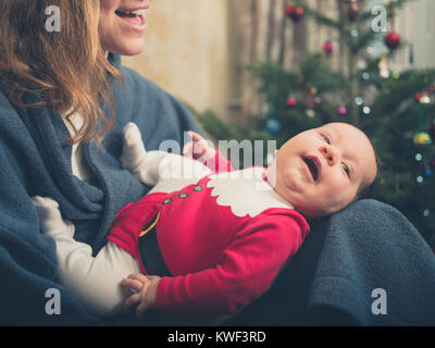 A happy baby wearing a santa outfit in front of the Christmas tree Stock Photo