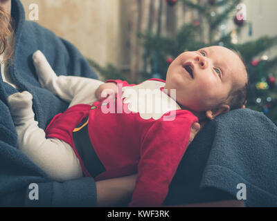 A happy baby wearing a santa outfit in front of the Christmas tree Stock Photo