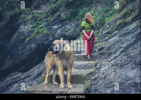 A young woman is walking up some steps outside in nature with her dog Stock Photo