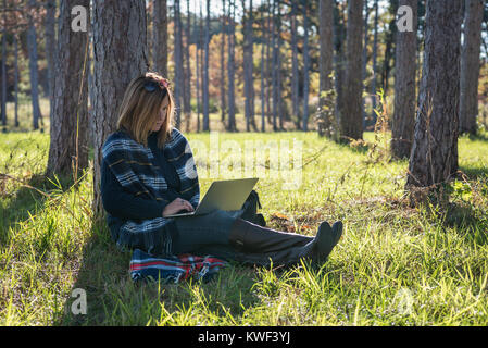 woman sitting against tree in forest using laptop computer Stock Photo