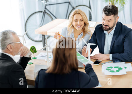 Smiling engineers. Enthusiastic creative smart engineers sitting together in their comfortable office and feeling enthusiastic while having tiny model Stock Photo