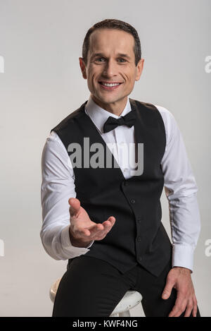 One minutes break. Joyful positive gay man smiling  on the chair while stretching hand and proposing to enjoy Stock Photo