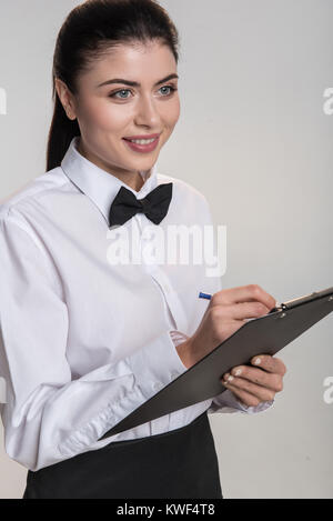 Anything else. Elegant pretty nice waitress posing on the isolated background while writing down order and smiling Stock Photo
