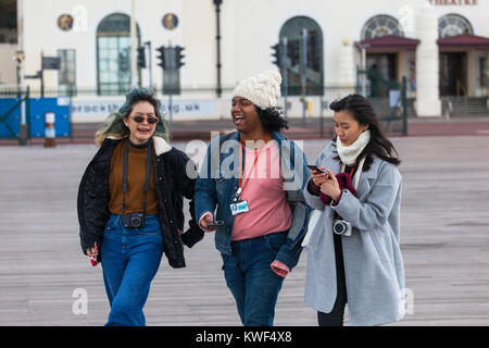 Three young students laughing and walking along the hastings pier, East Sussex Stock Photo