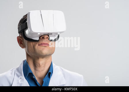 Virtual reality. Handsome professional male doctor wearing VR glasses while posing on the isolated background and trying modern technology Stock Photo
