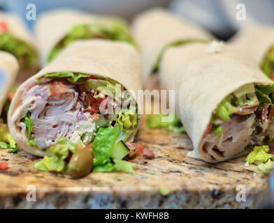 Yummy turkey wrap, tortilla around healthy vegetables and meats cut in half on a granite counter Stock Photo