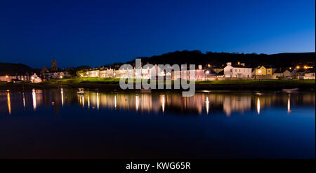 Row of colorful, quaint houses overlooking a harbor at dusk, with lights reflecting on the calm water Stock Photo