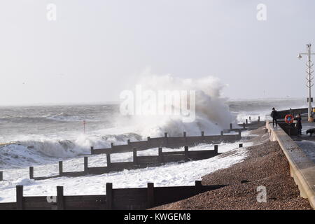 Bognor Regis, UK. 3rd January, 2018. Storm Eleanor: Passers-by on Bognor seafront  take advantage of the photo opportunity created by the backdrop of huge spray generated powerful Storm Eleanor waves crashing onto the beach at high tide. The shingle has been washed up unusually far between the groynes to the edge of the promenade. Stock Photo