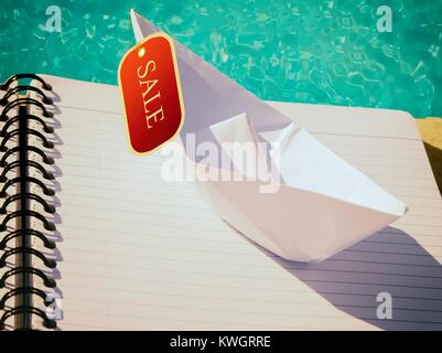 Origami boat placed on plain white  lined notebook with a sale tag hanging. Blue water in the background. Stock Photo Stock Photo