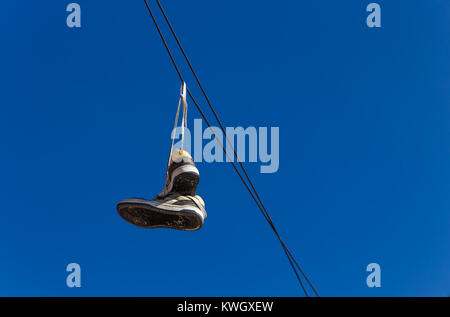 Pair of old sneakers hanging on an electric cable against a clear blue sky Stock Photo