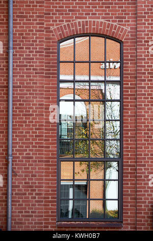 Tall arch format metal barn style window with small glazing pattern, in a red brick facade Stock Photo