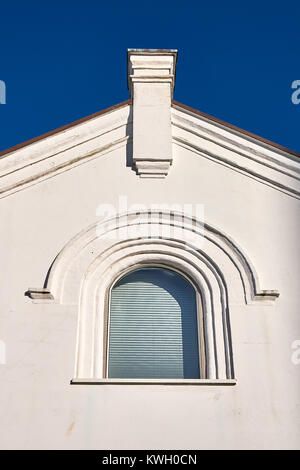 Arched window in a plastered triangled gable with a chimney rising against a blue sky Stock Photo
