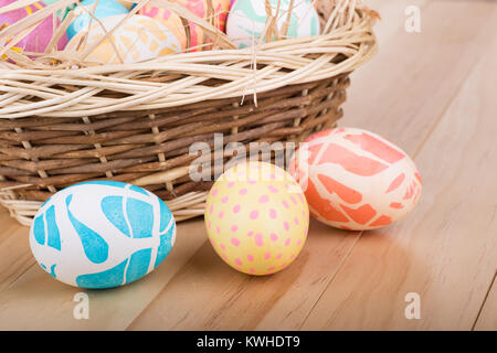 Colored Easter eggs on a wood surface in front of a basket Stock Photo