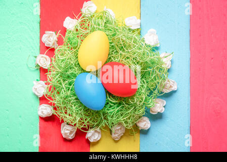 Easter arrangement with painted eggs on decorative grass, surrounded by small white roses, displayed on a background from multicolor wooden planks. Stock Photo