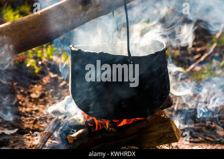 cauldron in steam and smoke on open fire. outdoor cooking concept. old fashioned way to make food Stock Photo