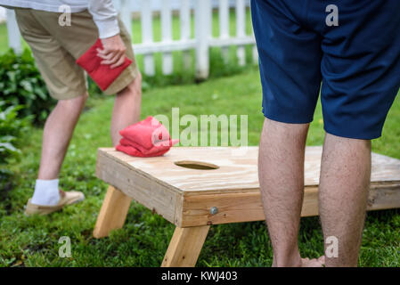 blurred action of two guys playing cornhole game in backyard Stock Photo