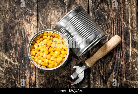 Canned corn in a tin can with opener. On a wooden background. Stock Photo