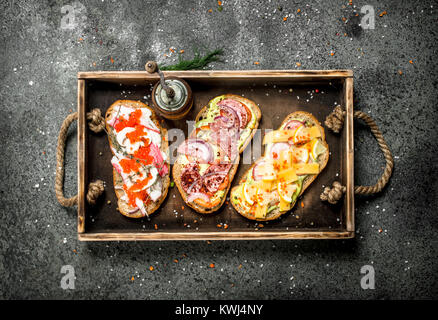 Various sandwiches with seafood, meat and vegetables on an old tray. On a rustic background. Stock Photo