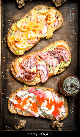 Various sandwiches with seafood, meat and vegetables on an old tray. On a rustic background. Stock Photo