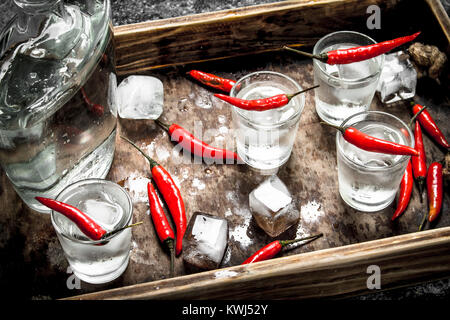 Vodka shots with chili peppers on a wooden tray. On a rustic background. Stock Photo