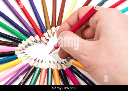 Man hand is prepared to write with a pencil inside the heart lined with pencils, isolated on white background Stock Photo