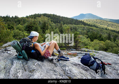 Hiker resting on rock outcrop on Long Trail, Vermont, USA. Camel's Hump mountain in distance. Stock Photo