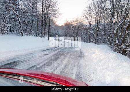 Icy slippery snow covered French alpine country road, with ice, after a blizzard, seen through the windscreen from inside the car at dusk. Alps France Stock Photo