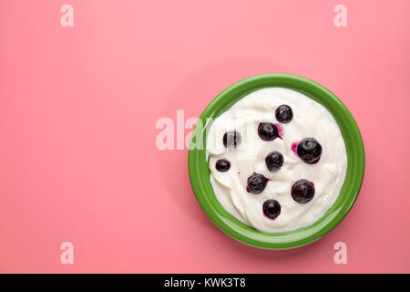 live organic Greek yogurt with vanilla and blueberries in a green ceramic bowl against pink background Stock Photo