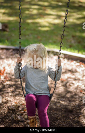 girl playing on swingset in park on a sunny fall day Stock Photo