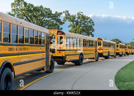 line of yellow school buses along curved drive outside of school Stock Photo