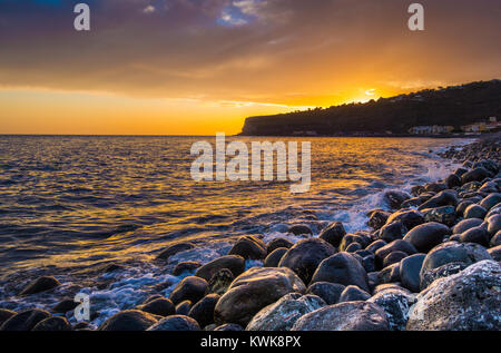 Panorama view of amazing ocean scenery with rocks on a beach in beautiful golden evening light at sunset with blue sky, clouds and sunlight lens flare Stock Photo