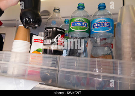 A drink trolley in the aisle on an Embraer 190 plane / aeroplane / airplane. Cabin crew are serving soft drinks to passengers during a flight. Stock Photo