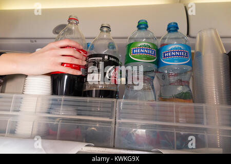 A drink trolley in the aisle on an Embraer 190 plane / aeroplane / airplane. Cabin crew are serving soft drinks to passengers during a flight. Stock Photo